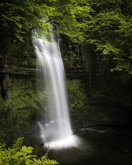 Fototapeta na wymiar Scenic vertical shot of the Glencar waterfall in a forest in Sligo, Ireland