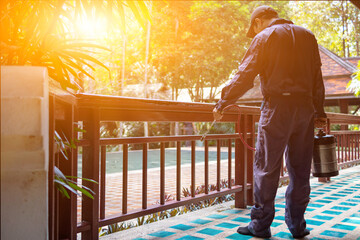 exterminate termite control company employee is using a termite sprayer at customer's house and searching for termite nests to eliminate. exterminate control worker spraying chemical insect repellant - Powered by Adobe