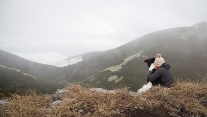 young red head woman sitting on a mountain top with czech mountain dog in the fog
