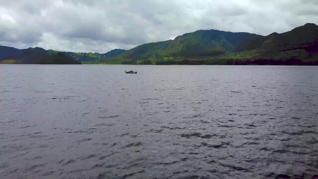 Motorboat on a lake surrounded by mountains, low aerial push in