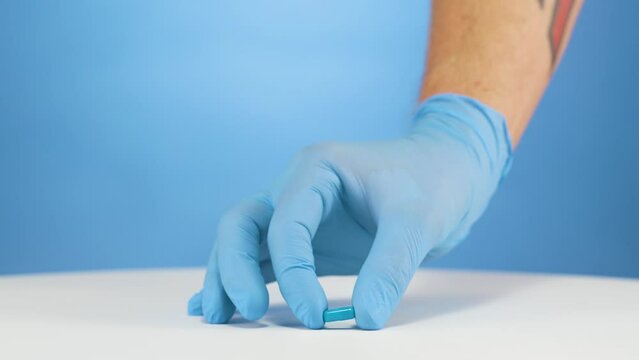 Hand with blue gloves carefully places blue vitamin, supplement pill on table