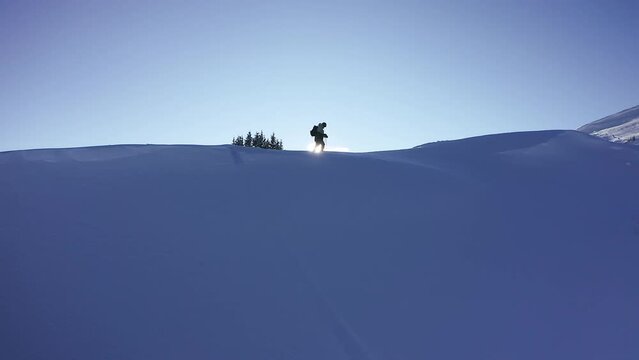 Aerial cinematic motion to the right featuring snowboarder split board hiking atop of mountain peak with sun flares scenic Mountain View during late sunset mid winter Vail Pass Colorado
