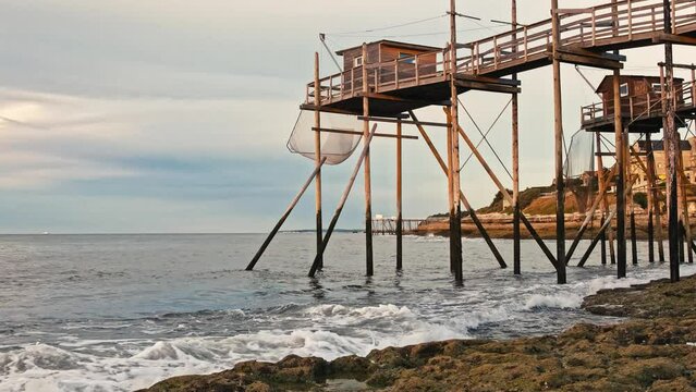 Rocky sea coast beach of Saint Palais in France with fishing hut and nets in sunset time. Ocean coast with constraction for fish catching and evening orange sky