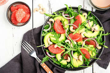 Vegan salad with arugula, avocado, grapefruit, cashew and olive oil, honey and wine vinegar dressing. White rustic table, top view, copy space