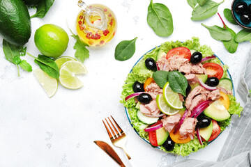 Fresh tuna salad with avocado, red tomato, cucumber, black olives, spinach, onion and lettuce. White table background, top view