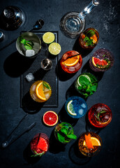 Cocktails set on black bar counter, top view. Mixology concept. Assortment of colorful strong and low alcohol drinks for cocktail party. Dark background, bar tools, hard light, top view