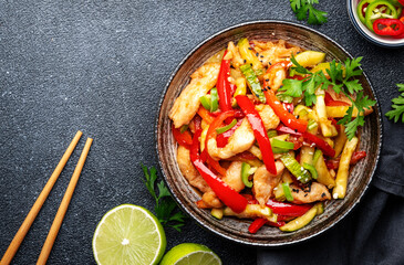 Asian cuisine, stir fry chicken, red paprika and zucchini with sesame and soy sauce in bowl. Black table background, top view, copy space