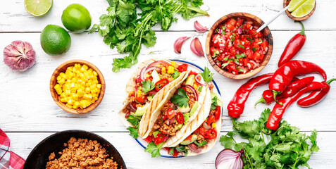 Tacos with beef, corn, red beans, tomato salsa sauce and red onions in corn tortilla on plate. Mexican cuisine. White table background, top view
