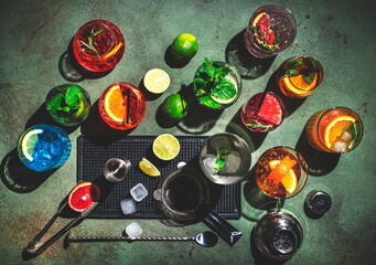 Cocktails set on rusty green bar counter, top view. Mixology concept. Assortment of colorful strong and low alcohol drinks for summer cocktail party. Dark background, bar tools, hard light