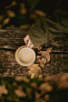 Fototapeta Top view of a hand holding a cup of coffee with milk on a wooden bench in autumn