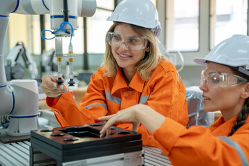 Female industrial engineer or technician working and inspecting robotic arm machine at manufacturing plant.