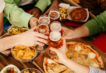 Friends with beer glasses at wooden table with delicious food - Top view having dinner toasting...