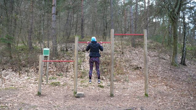 Static shot of women doing pull-ups on a bar in the forest for exercise