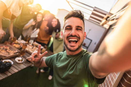 group of diverse young friends partying on rooftop eating and drinking alcohol selfie - focus on handsome guy smiling -