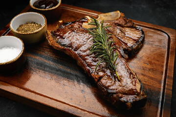 succulent grilled T-bone steak with rosemary and spices served on dark wooden board