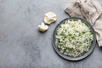 Raw cauliflower rice or couscous with dill on plate, healthy low carbohydrates vegetable side dish for keto diet and healthy low calories nutrition on grey concrete rustic background, copy space