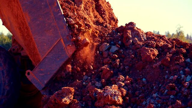 Follow close up shot of dump track dumping red and blue clay in pile. Then it drives away. The stones are crumbling. 25perc slow motion. 4k.