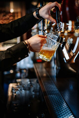man bartender hand at beer tap pouring beer in glass in bar or pub