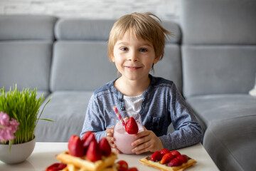 Sweet preschool child, boy, eating belgian waffle with strawberries and chocolate at home
