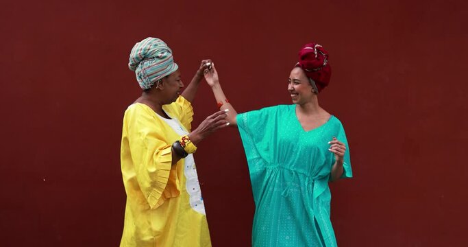 Happy african mother and her daughter wearing ethnic traditional dress while dancing together outdoor 
