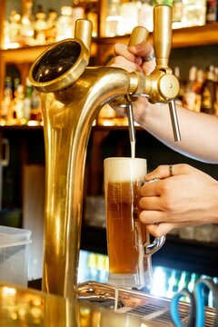 Vertical closeup of the bartender pouring beer from a beer tap.