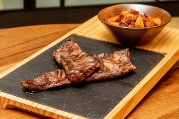 Pices of steak with fried potato on the wooden board.