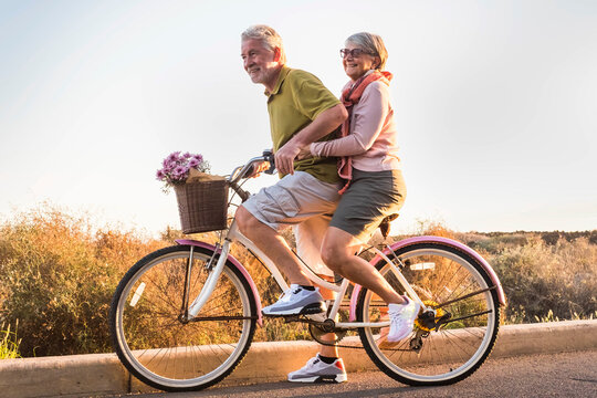 Healthy ad active mature retired people lifestyle. Man carrying woman senior aged on the same bike. Retired people having fun in outdoor leisure activity. Togetherness concept life. Happiness youthful