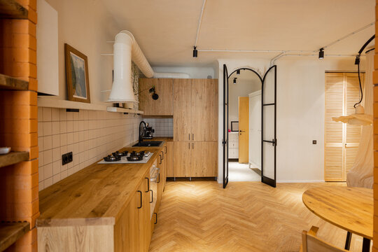 Photo of stylish kitchen interior made in wooden materials of modern studio apartment. Oak kitchen facades and metal arch door