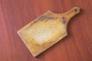 An old wooden board for cutting vegetables with knife scratches. Vintage kitchen appliance for cooking food.