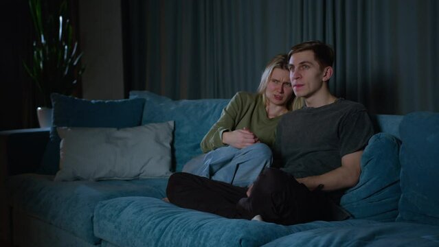 A young couple watching something scary on TV. beautiful couple spending time at home, sitting on a couch, watching scary TV Show in their stylish loft apartment.