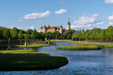Obraz premium View through the palace gardens towards Schwerin Palace. Reflection in the water. Sunny day with light clouds.