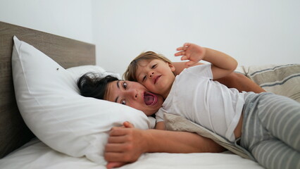 Mother and child laying in bed smiling. Happiness motherhood lifestyle concept. Little boy hugs mom cheek to cheek