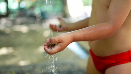 Child washing hands outside during heat day. Refreshing water during summer day. Little boy wearing bathing suit brief