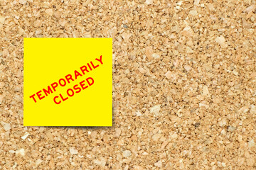 Yellow note paper with word temporarily closed on cork board background with copy space