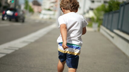 Back of happy active child running in city street sidewalk during sunny summer day