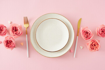 Flat lay photo of empty plate cutlery knife fork flowers pink peony rose buds and small hearts on...