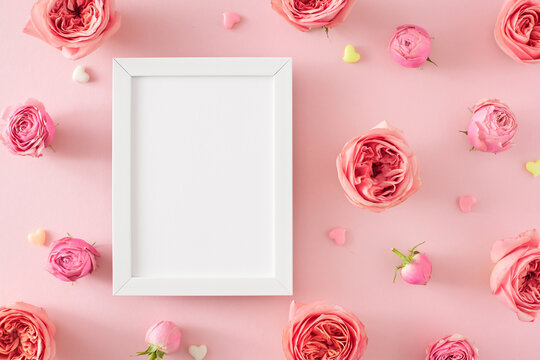 Flat lay photo of empty photo frame and natural flowers pink rose buds and small hearts on isolated pastel pink background. Mother Day atmosphere concept