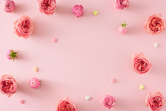 Top view photo of flowers pink rose buds and small hearts baubles on isolated pastel pink background with empty space in the middle. Happy Mother Day concept