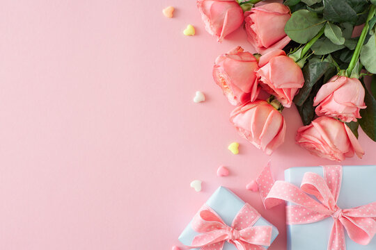Mother Day mood concept. Flat lay photo of present boxes with bows bunch of pink roses and small hearts baubles on isolated pastel pink background with empty space