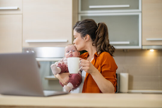 Young woman working on laptop with her baby at home