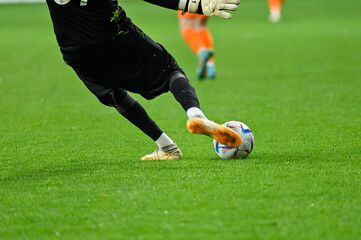 Football goalkeeper kicks ball. Player's legs and the ball during soccer match.