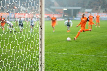 Detail of goal's post with net and football player during penalty kick in the background.