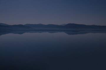Fototapeta na wymiar Silhouette of mountains near lake at the early morning with clear sky
