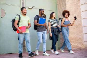 A diverse group of college students. Happy casually dressed multiethnic young friends with textbooks and backpacks. The 4 young people leave through the door of the university. School break concept.