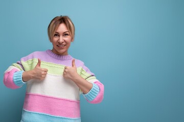 smiling blond woman in casual outfit showing ok gesture on blue background with copy space