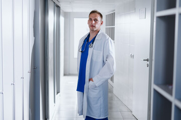 Portrait of a man in a blue surgical suit and a white coat in a hospital locker room.