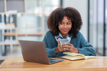 Fototapeta premium Beautiful young smiling woman with curly hair working on laptop and drinking coffee sitting at cafe.