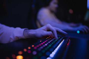 Cropped view of gamer using keyboard with colorful lighting in gaming club.