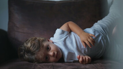 One bored small boy lying on couch twisting and turning. Child laid on sofa at home with nothing to do feeling boredom. Childhood lifestyle