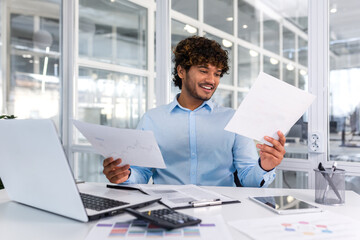 Successful financier accountant working inside office with laptop and documents, man satisfied with audit results smiling and reading financial reports, businessman using laptop for paperwork.